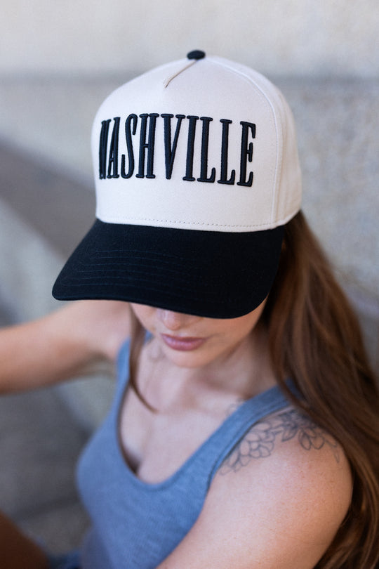 Person wearing a cream and black Nashville snapback hat with bold raised lettering