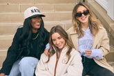 Three women sitting on steps wearing casual clothing and hats.