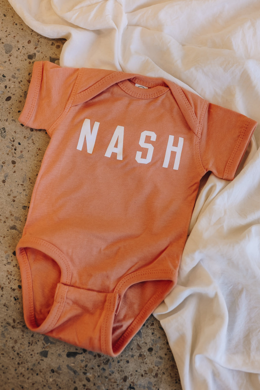 Orange baby onesie with NASH on the front.