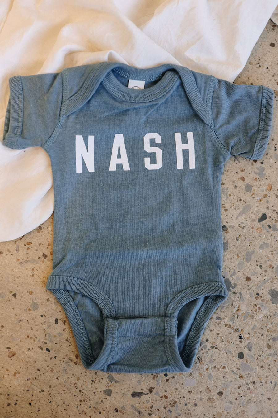 Indigo blue baby NASH onesie with snap closure.