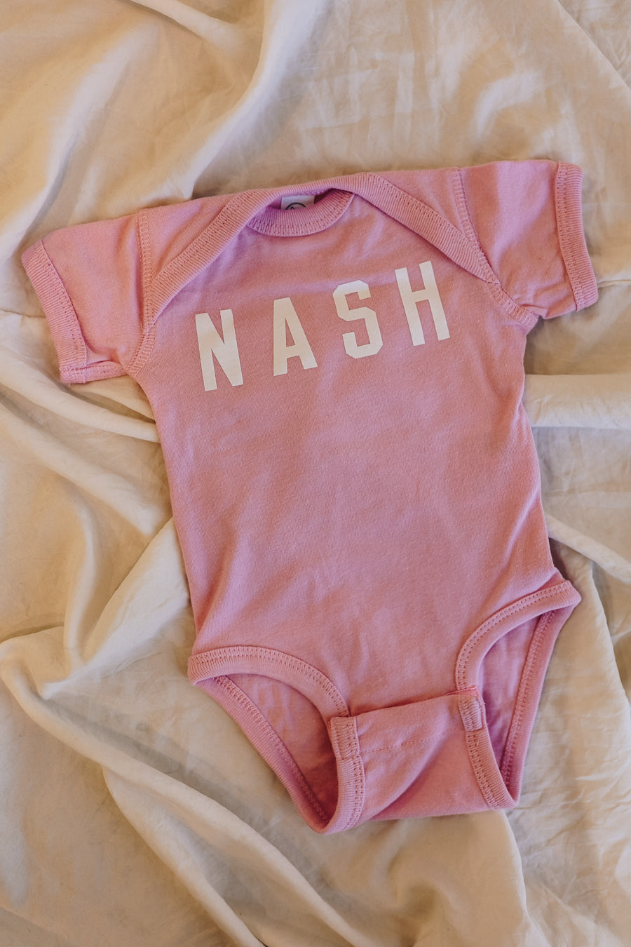 Light pink baby onesie with NASH on the front. 