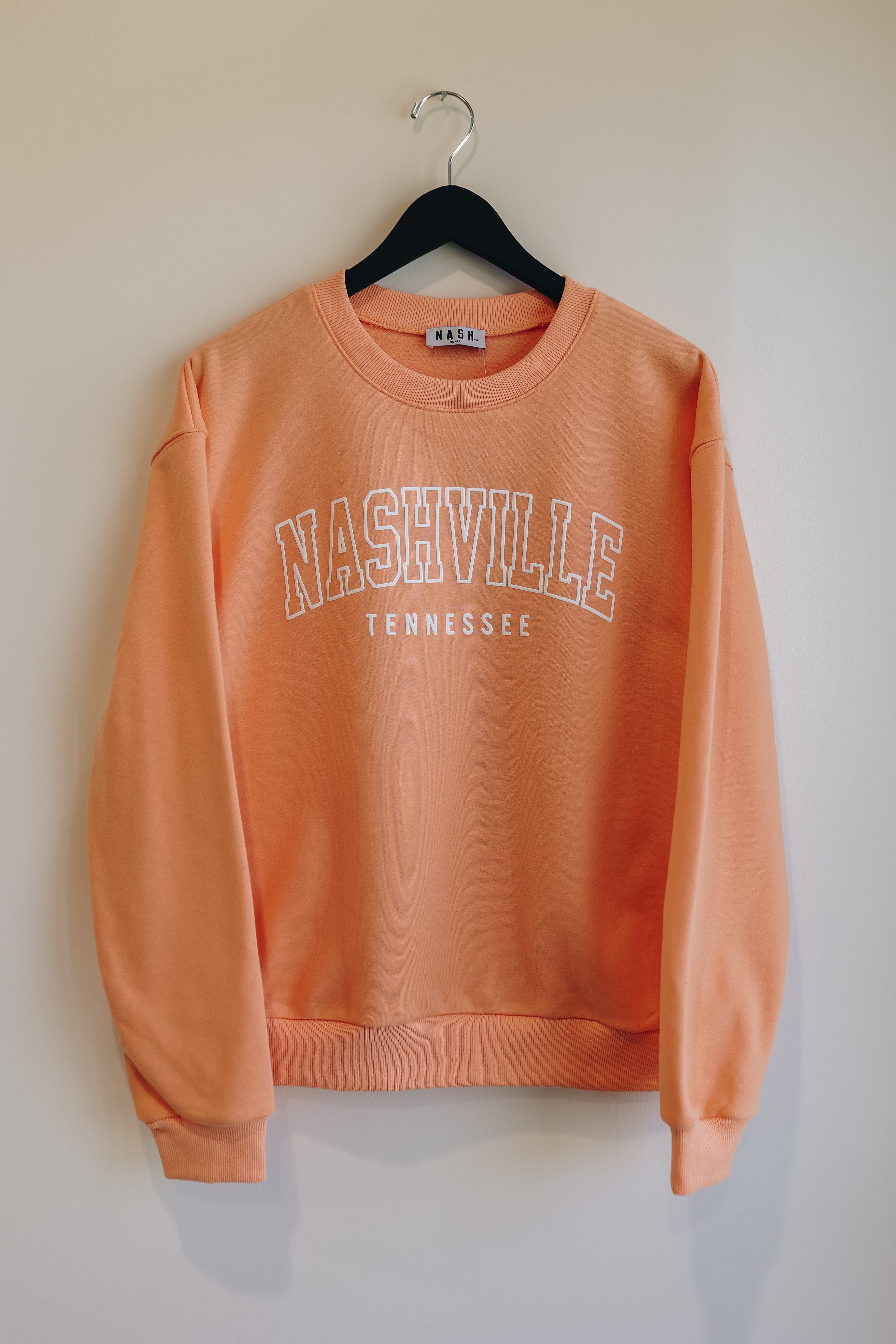Bright apricot color sweatshirt with collegiate puff ink Nashville on the front